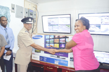 Junior Public Infrastructure Minister Annette Ferguson (right) handing over a 48-inch monitor from the Demerara Harbour Bridge to Commissioner of Police Seelall Persaud  