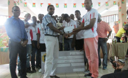 Captain of Federal Winners Connection Marlon Maxius (right) collecting the championship trophy from GT Beer Brand Manager Geoff Clement while the UDFA President Sharma Solomon (left) and members of the team look on
