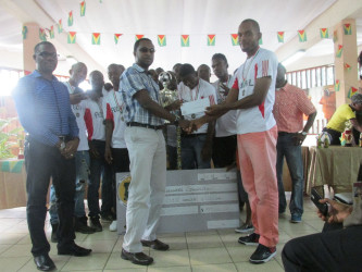Captain of Federal Winners Connection Marlon Maxius (right) collecting the championship trophy from GT Beer Brand Manager Geoff Clement while the UDFA President Sharma Solomon (left) and members of the team look on 