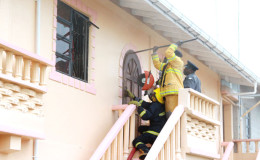 Firemen yesterday prying the door open to gain access to the house. (Photo by Keno George)
