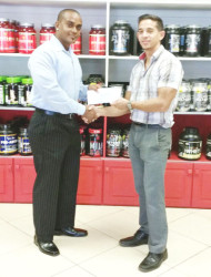 CEO of Fitness Express, Jamie McDonald hands over the sponsorship cheque to PRO of the Guyana Amateur Powerlifting Federation (GAPF), Roger Callender to aid in this year’s Novices Powerlifting Championships. 
