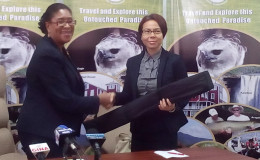 Minister of Public Telecommunications and Tourism Cathy Hughes handing over a poster to An Yin Choo, Head of Diaspora, Ministry of Foreign Affairs, while Gerry Gouveia sits at far left. The head table’s backdrop is one of the retractable posters.