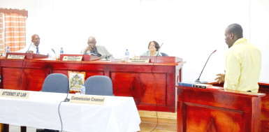 Dwayne Lewis on the stand offering testimony before the members of the Commission of Inquiry into the Camp Street prisoner deaths. From left are Dale Erskine, Commissioner, Justice James Patterson, Chairman, and Merle Mendonca, Commissioner. 