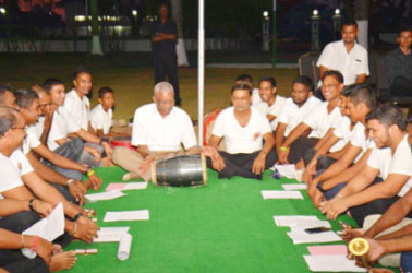 President David Granger (centre) knocking a drum as the chowtal singers watch on (Ministry of the Presidency photo) 
