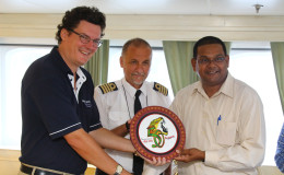 Cruise Director Neil Horrocks (left) and Captain of the ship Etien Bonacic (centre) were also presented with several tokens including this piece bearing Guyana’s 50th Anniversary logo.