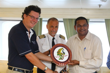 Cruise Director Neil Horrocks (left) and Captain of the ship Etien Bonacic (centre) were also presented with several tokens including this piece bearing Guyana’s 50th Anniversary logo.  