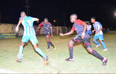 Jamal Gibbs (12)  in the process of initiating a left side cross while being pursued by Joshua Brown (right) and Dwight Peters (left) of Alpha United during their GFF Stag Beer Elite League matchup