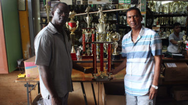 Chairman of the Boyce/Jefford Committee, Colin Boyce (left) receives some of the trophies yesterday that will be up for grabs on Sunday from Proprietor of the Trophy Stall, Ramesh Sunich.