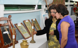 First Lady, Sandra Granger (right) takes a closer look at one of the candlesticks displayed at an exhibition hosted by the Dharm Shala as Kella Ramsaroop, Managing Director of the facility, explains its history. (Ministry of the Presidency photo)