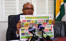 Opposition Leader Bharrat Jagdeo holding up a government advertisement highlighting its achievements over the last year.