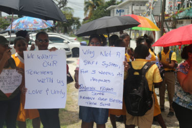 Some of the parents holding placards which demonstrated their dissatisfaction with the relocation and reassignment of teachers and students prior to the decision being reversed by the Ministry of Education yesterday afternoon. (Photo by Keno George)     