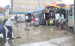Parliament View Mall vendors yesterday morning trying to remove water lodged in their vending space following rainfall overnight. (Photo by Keno George) (See story on page 9)
