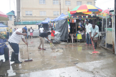 Parliament View Mall vendors yesterday morning trying to remove water lodged in their vending space following rainfall overnight. (Photo by Keno George) (See story on page 9) 