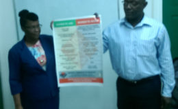 A member of the NCD alongside John Adams, advisor to the Minister of Social Protection, holding up a disability etiquette poster.
