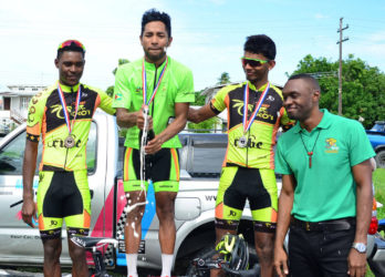 Geron Williams pops a bottle of champagne on the podium with second place finisher, Raynauth Jeffrey (right) and Stephano Husbands both of Team Coco’s. (Orlando Charles) 