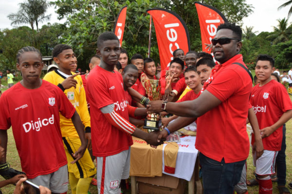 Captain of Mahdia Secondary Travis Caesar (left) collects the trophy for the winning team from Digicel representative Shawn Weatherspoon after their defeat of Paramakatoi Secondary Saturday.