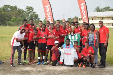 Wismar/Christianburg captain Keshawn Dey collecting the championship trophy from Digicel Representative Mario Grimshaw while other members and supporters of the team look on following their win over Kwakwani Secondary in the Region 10 Final of the Digicel Schools Football Championship