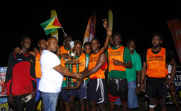 Captain of the victorious Tucville unit Delon Williams (centre) collects the championship trophy from Petra Organization Director and event coordinator Troy Mendonca while other members of the celebrate following their win over North East La Penitence in the Ministry of Health Soft Shoe Championship Finale at the Ministry of Education Ground. (Orlando Charles photo)