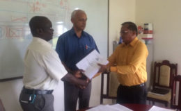 Minister of Communities Ronald Bulkan (centre) looks on as Permanent Secretary Emil McGarrell (left) hands over the contract to Managing Director of Puran Brothers Disposal Inc. Lakenauth Puran after it was signed.