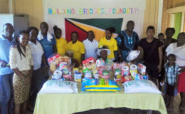 The elderly women (seated behind food items), pose with members of Building Bridges Foundation and others. 