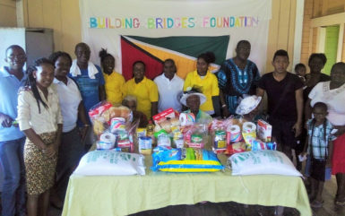 The elderly women (seated behind food items), pose with members of Building Bridges Foundation and others. 