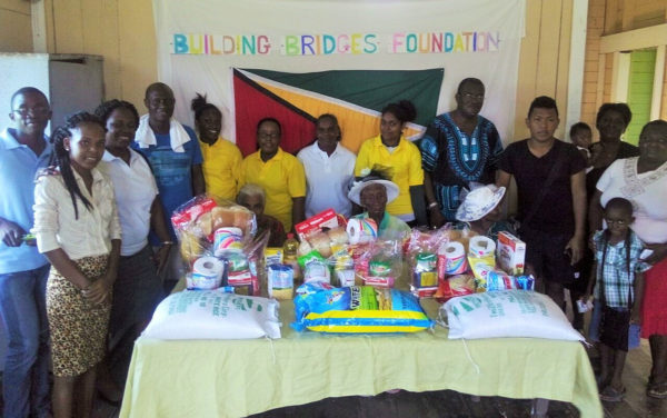 The elderly women (seated behind food items), pose with members of Building Bridges Foundation and others. 