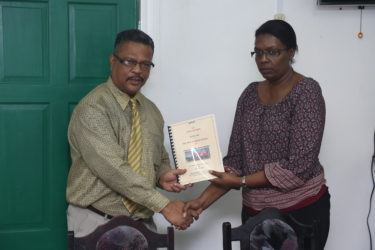 Chief Labour Officer Charles Ogle (left) hands over the report to Human Resources Manager of John Fernandes Limited Donna Roberts Benjamin 