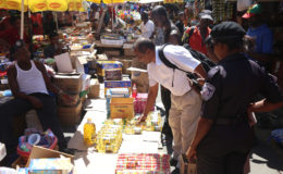 Chief Meat and Food Inspector Deonarine Arjune confiscates several bottles of cooking oil as a city constable looks on.
