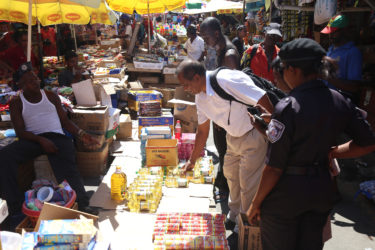 Chief Meat and Food Inspector Deonarine Arjune confiscates several bottles of cooking oil as a city constable looks on. 