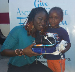 Cultural Ambassador of Give Another Chance Foundation, Melissa “Vanilla” Roberts handing over footwear and backpack to a child.