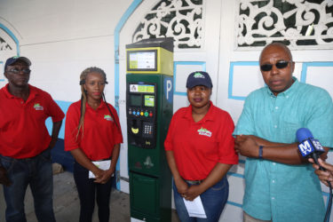 Smart City Solutions Director Ifa Kamau Cush (right), a key player behind the parking meters contract, with one of the proposed meters and his assistants during a demonstration at City Hall in June. 