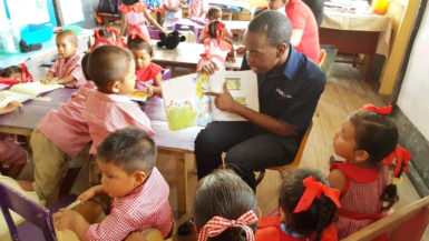 A Digicel employee reading to a group of students from the St. Cuthbert’s Mission Nursery School as part of a World Literacy Day activity on Thursday. (Digicel Guyana photo)