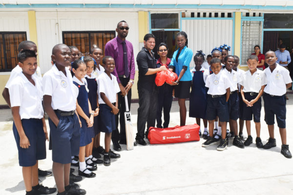 Stella Maris Primary School Headmistress Shivanie Singh receives some cricket gear from Ramnaresh Sarwan, in the presence of students and a teacher. NSC’s Christopher Jones is to the left of Sarwan.