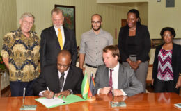 Minister of State Joseph Harmon signs the agreement as Germany’s Regional Director for Latin America and the Caribbean Ambassador Dieter Lamle (seated at right) looks on at the Ministry of the Presidency yesterday. Also looking on are (from left) Honorary Consul of Germany to Guyana Ben ter Welle, Germany’s Ambassador to Guyana Lutz Hermann Gorgens, Commissioner of the Protected Areas Commission (PAC) Damian Fernandes, Ms. Ndibi Schwiers-Ceres and Deputy Commissioner of the PAC Denise Fraser. (Ministry of the Presidency photo)