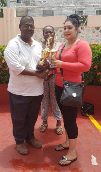 In picture president of the Guyana Draughts Association Jairam is seen receiving the trophies from a representative of the Berbice Bridge Inc., while the secretary of the GDA Marlyn Ali looks on.