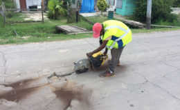 One of the workers cutting around one of the potholes in the road. 