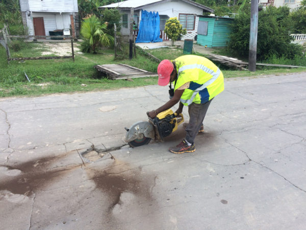 One of the workers cutting around one of the potholes in the road. 