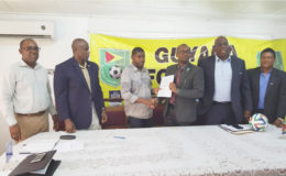 GFF President Wayne Forde (3rd from right) handing over the signed contract to Dwain Ferdinand of Home Designs and Engineering Associates while FIFA Development Officers Howard McIntosh (2nd from right) and Anton Cornel (right) alongside GFF Vice Presidents Rawlston Adams (left) and Bruce Lovell (2nd from left) look on