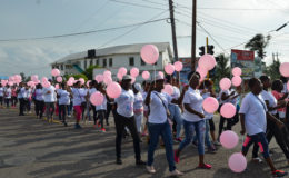 Participants carrying pink balloons, walk along Camp Street in Joshua Singh of Fit-Rex gym during the warm-up exercises