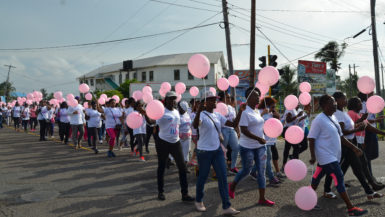 Participants carrying pink balloons, walk along Camp Street in Joshua Singh of Fit-Rex gym during the warm-up exercises