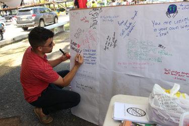 Tommy Lee, LGBT Coalition Development Specialist at SASOD, writes a charge to individuals to love themselves. This board, open to individuals to leave messages of encouragement, was placed on Main Street yesterday as part of the Youth Advocacy Movement’s Anti-bullying campaign. (Photo by Keno George)