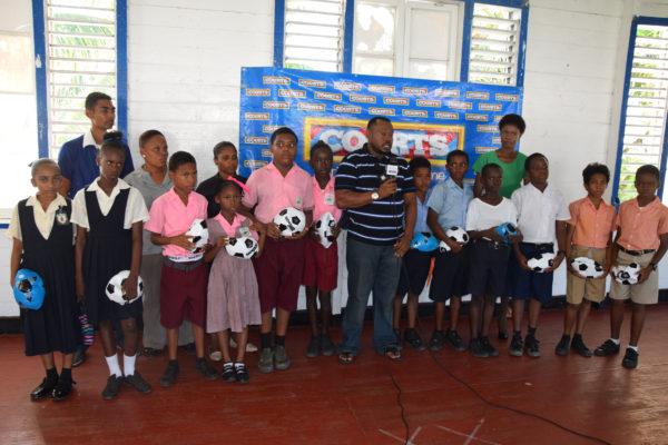 Students of the participating schools in the 5th Annual Courts Pee Wee Football Championship displaying their donated footballs from the Petra Organization while Co-Director Troy Mendonca (centre) of the aforesaid entity addresses the media gathering. 