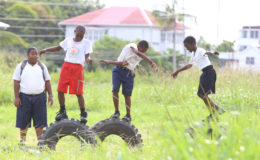 Schoolchildren attempt to see who can remain standing the longest on old tyres they found in a weed-filled ground opposite Stella Maris Primary School on Tuesday. (Photo by Keno George)