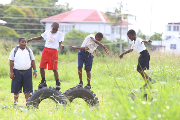 Schoolchildren attempt to see who can remain standing the longest on old tyres they found in a weed-filled ground opposite Stella Maris Primary School on Tuesday. (Photo by Keno George)