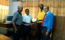 Treasurer of the Guyana Olympic Association (GOA) and former national table tennis junior champion Garfield Wiltshire hands over the sponsorship cheque to Kaysan Ninvalle while national coach Linden Johnson and GOA president K Juman Yassin look on.