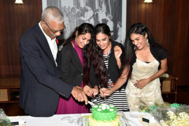 President David Granger sticks the birthday cake with (from left) Radha Mansaram, Rajshri Mansaram and Reenica Mansaram. (Ministry of the Presidency photo)    