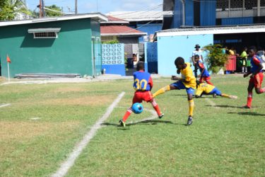Timely interception-A St. Agnes defender (blue) makes a last ditch block on an attempted shot from a West Ruimveldt striker during their semi-final encounter at the Thirst Park ground in the 5th Annual Courts Pee Wee Football Championship