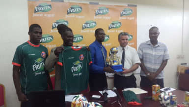 Club Secretary (centre) Daniel Thomas collecting the symbolic trophy from Guyana Beverage Company Incorporated (Inc.) Chief Mark Telting (2nd from right) while Head-Coach Sampson Gilbert (2nd from left), displays the new team kit alongside U17 Captain Jeremy Garrett (left) and GFF Executive Dion Innis at the Guyana Beverage Company Headquarters in Diamond