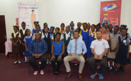 Students from the participating primary schools are all smiles at the launch of the 3rd Annual Smalta Girls Pee Wee Football Championship, in the presence of (sitting from left to right) Petra Organization Co-Director Troy Mendonca, Joy Gravesande, Health Officer of the Ministry of Public Health, Smalta Representative Sean Abel, and Nicholas Fraser, Head of Physical Education Department of the Ministry of Education 