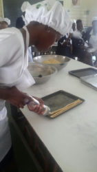 A student pumps out rows of cheese straw dough for baking.